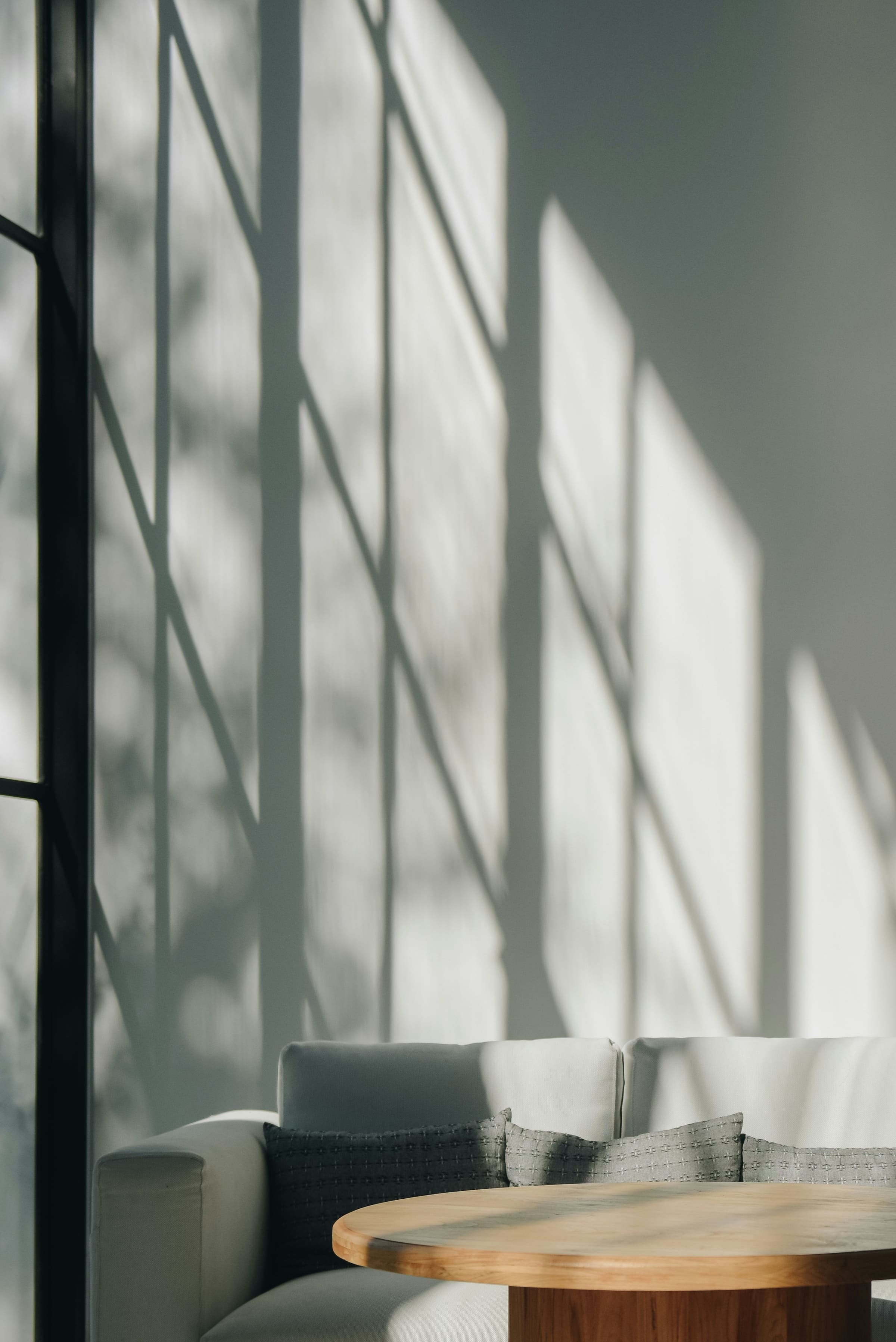 Afternoon light falling across a pale wall above a low sofa and a round timber table.