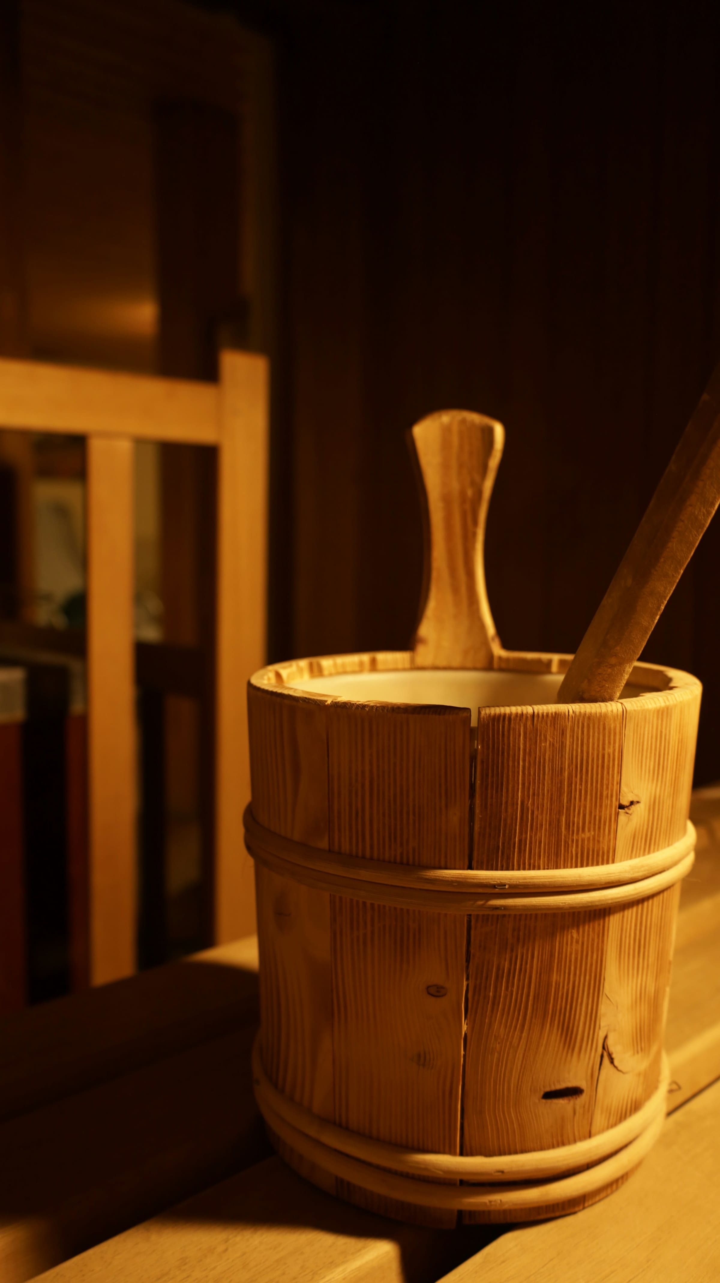 A wooden pail and ladle resting on a timber bench in a warm treatment room.